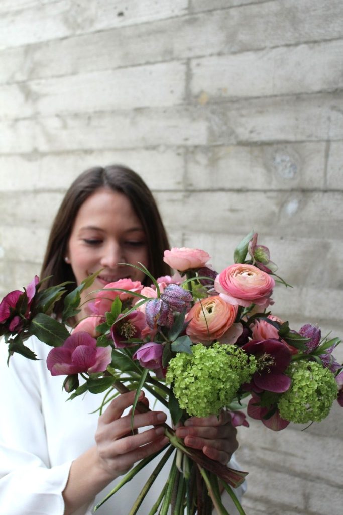 Eine Person hält einen bunten Blumenstrauß, umgeben von einer grauen Wand.