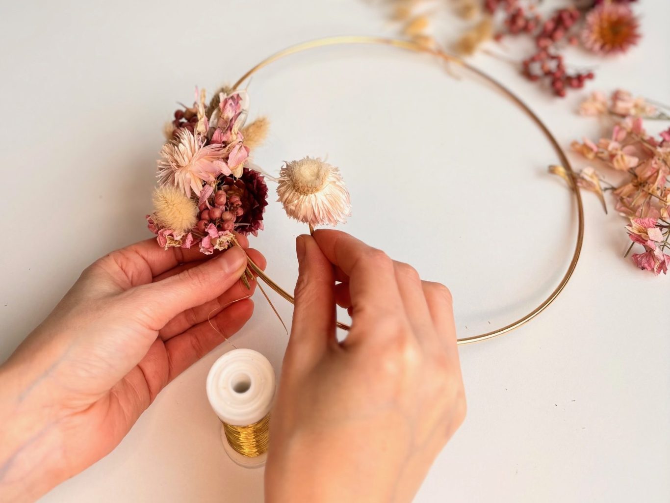 Teamevent in München, Kranz binden mit Trockenblumen, Florales Design Hände fügen Trockenblumen einem goldenen Drahtring hinzu.