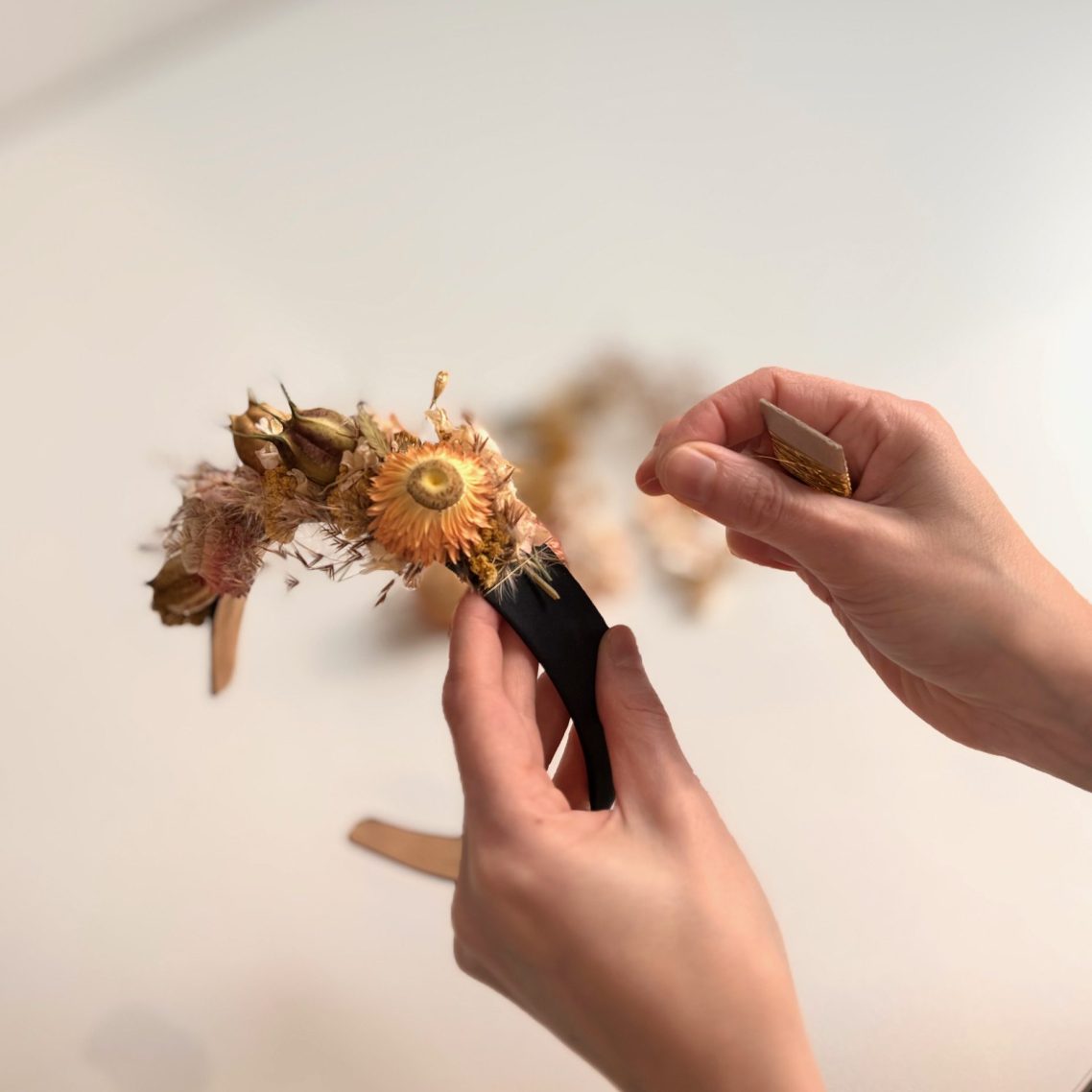 Blumenworkshop München mit Trockenblumen, Florales Design Hände halten eine Haarreif und binden gelbe getrocknete Blumen darauf.